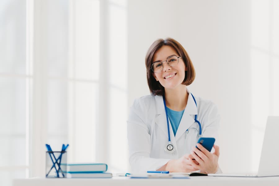 Eine Ärztin sitzt in Ihrem Büro und hält Ihr Mobiltelefon in der Hand und nutzt die Healthapp.