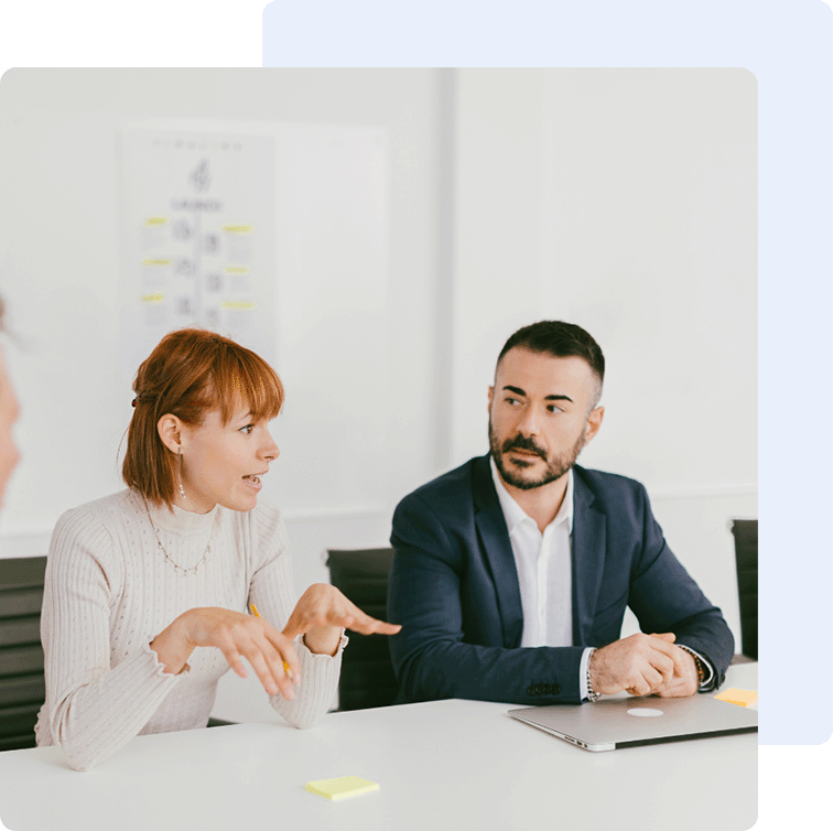 Text im Bild. Im Bild sind eine Geschäftsfrau mit kurzen orangen Haaren sowie ein junger Mann im Anzug zusehen. Es scheint als wäre es in einer Sitzung.